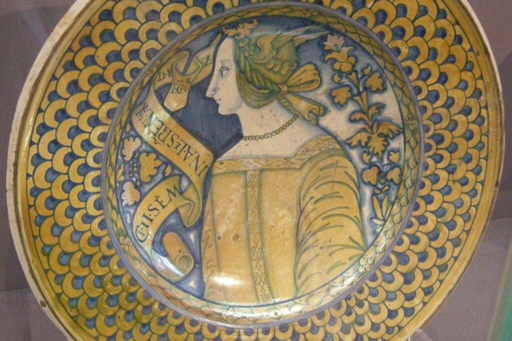 Piatto di maiolica di Deruta del 1520 circa: al centro il busto di una donna, intorno una decorazione a squame gialle e azzurre.